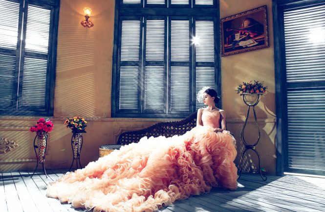 Frau sitzt in gigantischem Kleid in einem mediteran anmutendem Zimmer, schaut nach links.